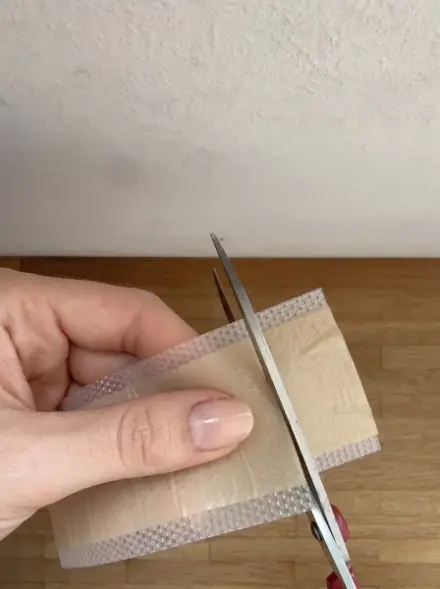 Ein Stück wird mit der Schere von der Narbenpflaster-Rolle abgeschnitten